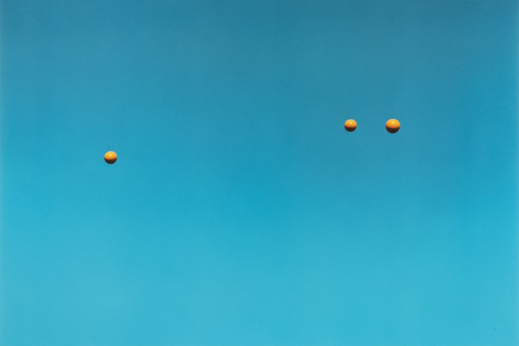 Three yellow balls floating against a clear blue sky